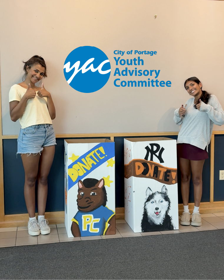 Two Youth Advisory Committee members stand next to food drive bins.